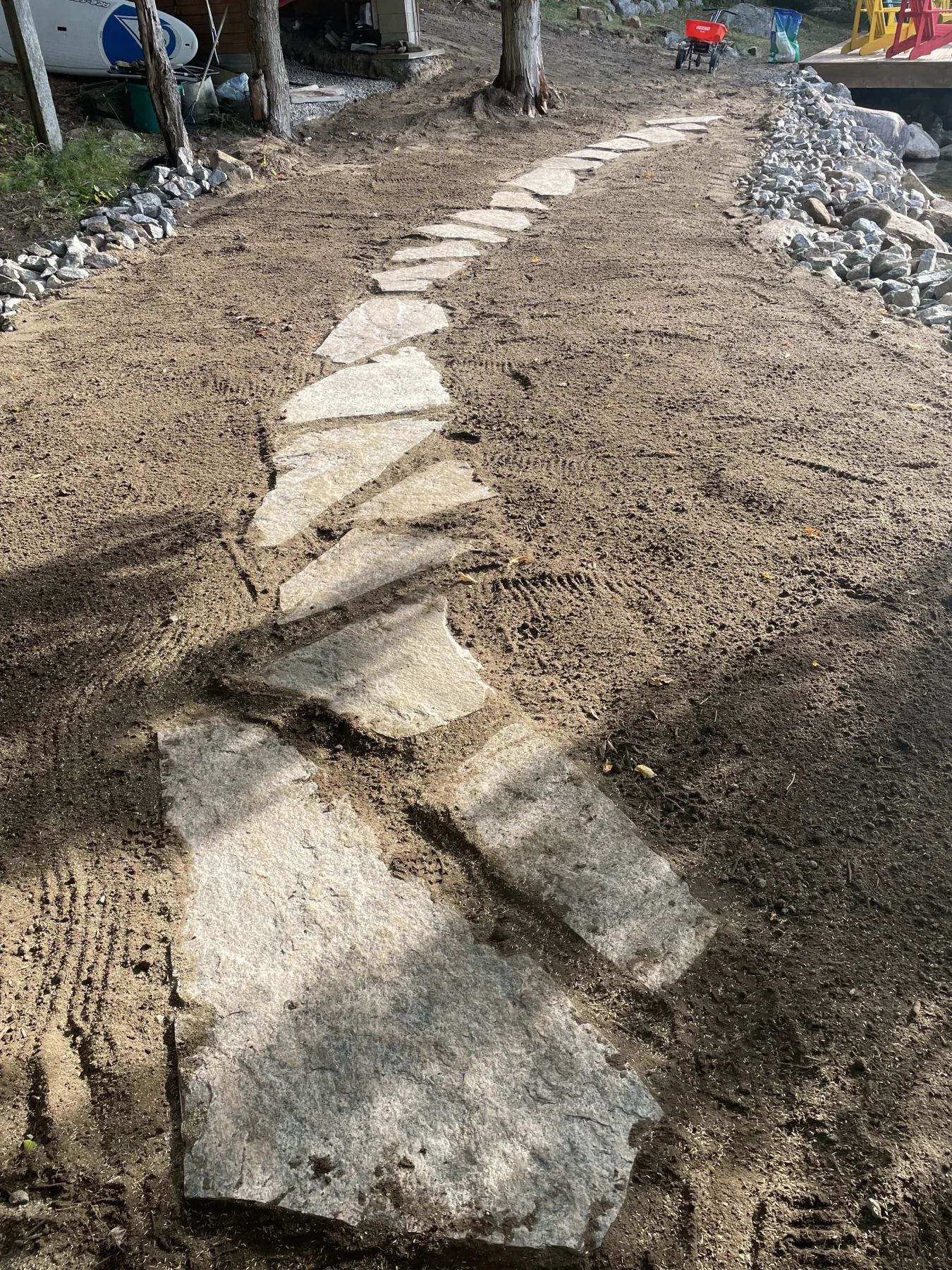 Hand-fit flagstone walkway being installed by Bouwers Design Landscaping at a North Bay cottage property, with a fresh pile of stones staged for the next section.