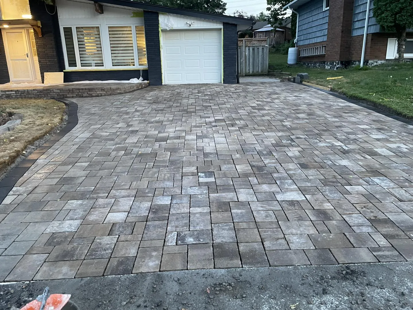 Completed interlock driveway replacement by Bouwers Design Landscaping in North Bay, Ontario, framed against the garage entry and side stair landing.