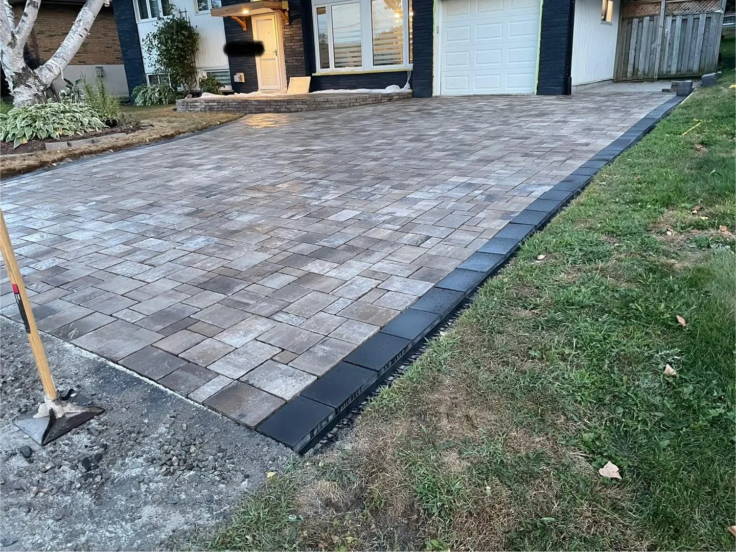 Finished Bouwers Design Landscaping interlock driveway in North Bay, Ontario, laid in Permacon Trafulgar pavers with Margeau Beige border, photographed at golden hour.