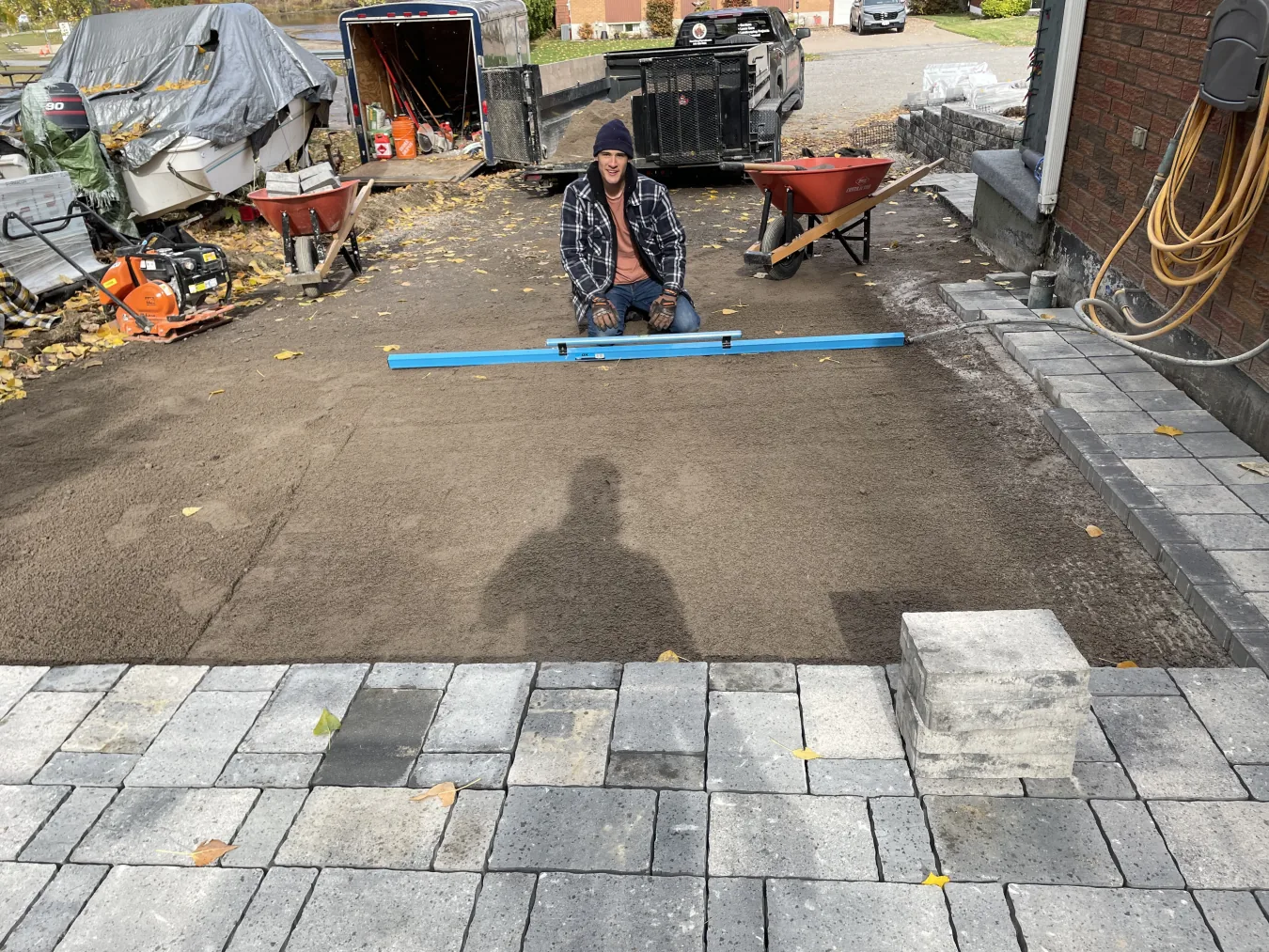 Bouwers Design Landscaping crew member screeding the HPB aggregate base on a Permacon Trafulgar Newport Grey paver install in North Bay, Ontario, with the paver field partially set in the background.